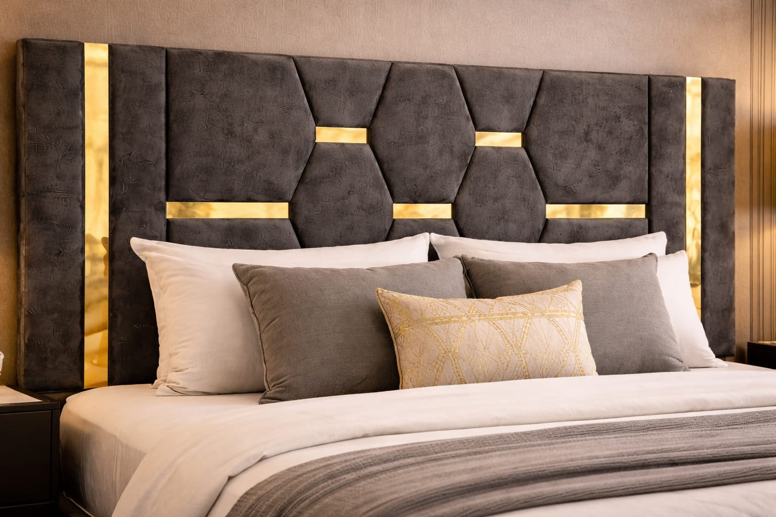 Gray upholstered headboard with gold accents and decorative pillows on a bed.